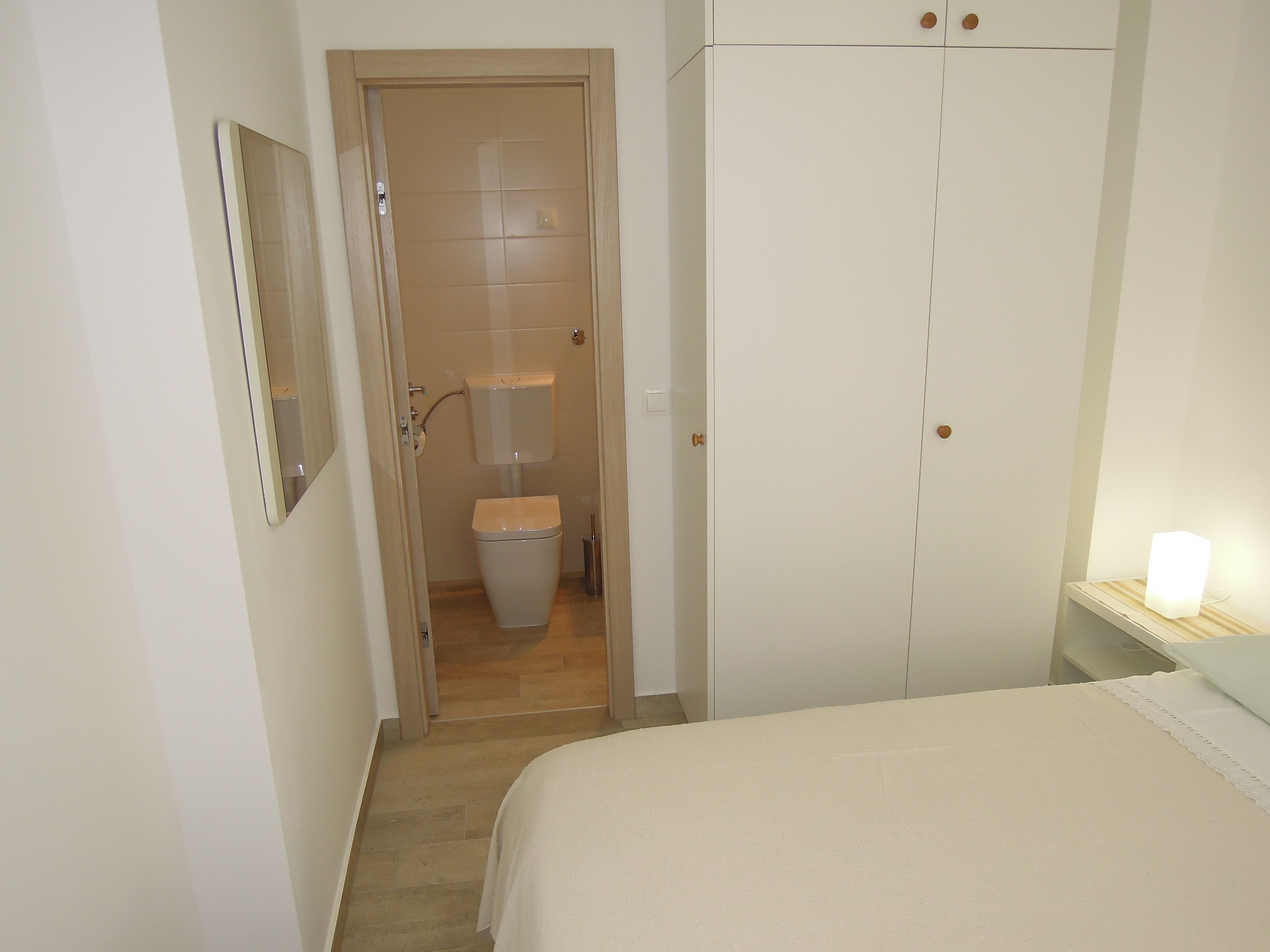 Un dormitorio con cama, armario y baño con inodoro y lavamanos.