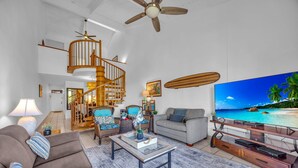 Ein geräumiges Wohnzimmer mit einer Holztreppe, einem großen Flachbildfernseher und Blick auf einen Strand.