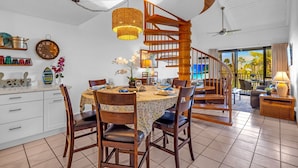 Ein Essbereich mit einem runden Tisch, Stühlen und einer Wendeltreppe, die zu einem Balkon mit Blick auf Palmen führt.