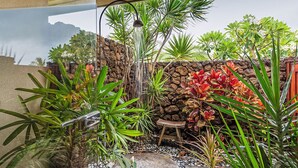 A tropical garden with a stone wall, a small wooden table, and various plants. - Oceanview Mauna Kea Luxury Villa - Private Pool & Spa - In-home Chefs Available (Waimea)