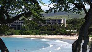 A beach with clear blue water, people swimming and sunbathing, and a building with multiple floors in the background. - Oceanview Mauna Kea Luxury Villa - Private Pool & Spa - In-home Chefs Available (Waimea)