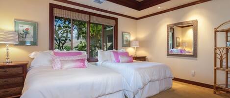 A bedroom with two beds, a ceiling fan, a large window with curtains, and a mirror on the wall.