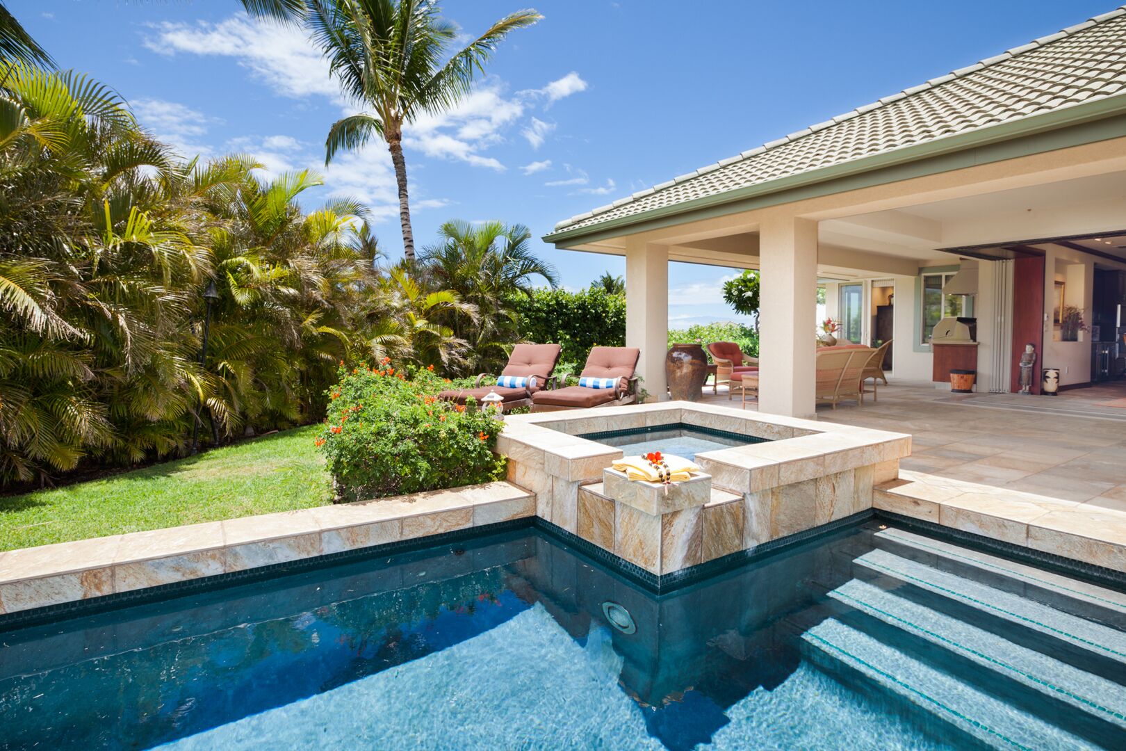 A swimming pool with a hot tub, surrounded by palm trees and a covered patio area.