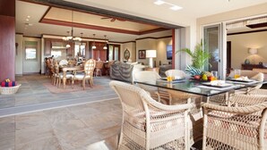 A spacious dining area with a glass table and wicker chairs, a kitchen in the background, and a large window with a view. - Oceanview Mauna Kea Luxury Villa - Private Pool & Spa - In-home Chefs Available (Waimea)