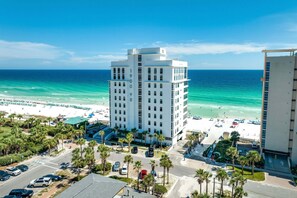 Un hôtel de grande hauteur offrant une vue sur la plage, avec de nombreux étages et un parking où sont stationnées des voitures.