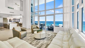 A spacious living area with a large window overlooking the ocean, a modern kitchen, and a seating area with a round coffee table.