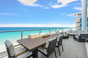 Un balcon avec une table et des chaises en bois, un canapé et une vue sur l’océan.