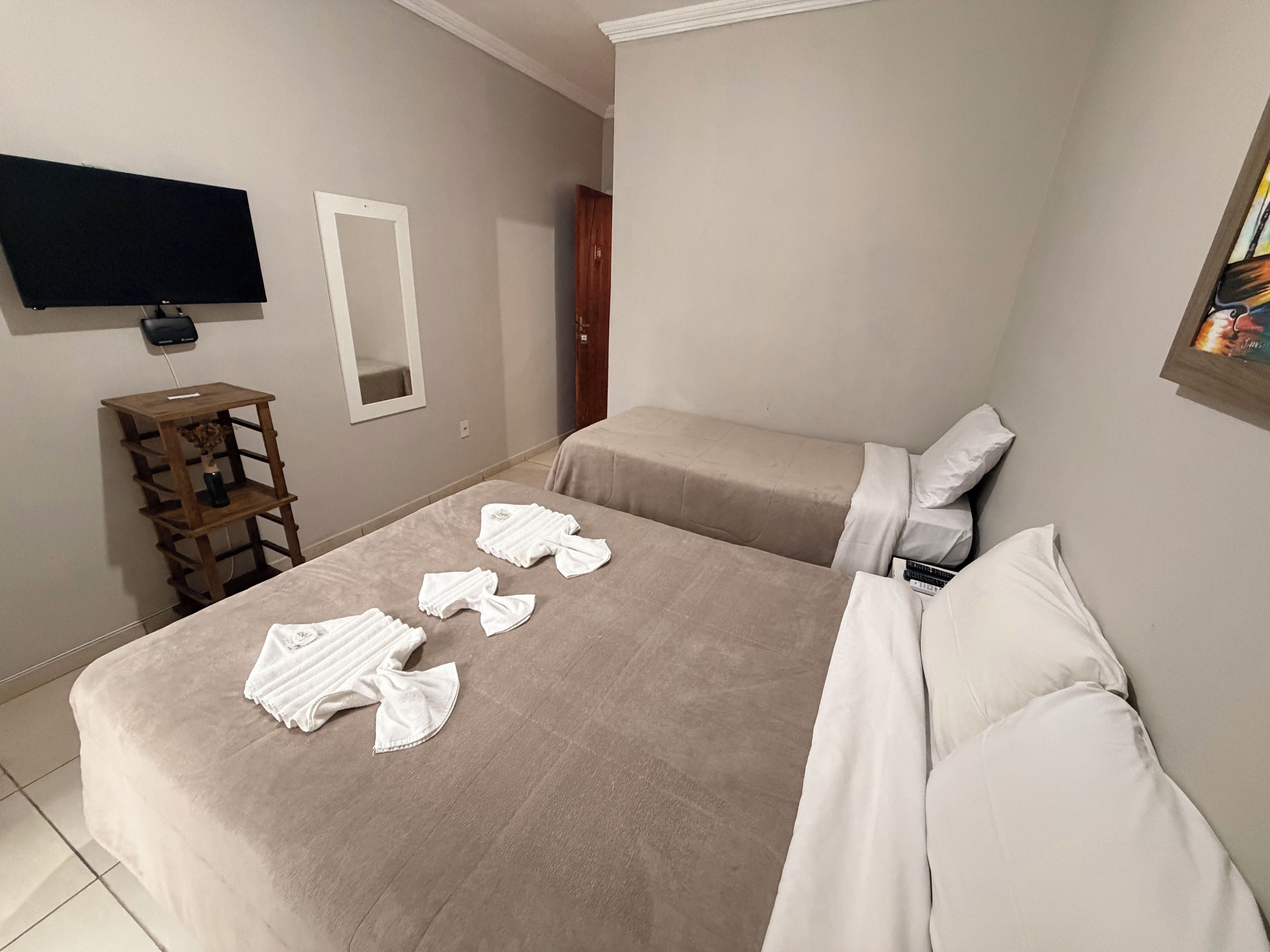 A hotel room with a bed, a TV mounted on the wall, a wooden shelf, and a door.