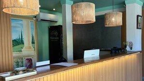Bancada de recepção com acabamento em madeira e um monitor Samsung. Três grandes luminárias pendentes de vime estão suspensas acima.