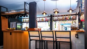 Uma área de bar com balcão de madeira, banquetas pretas, luminárias pendentes e prateleiras com garrafas.