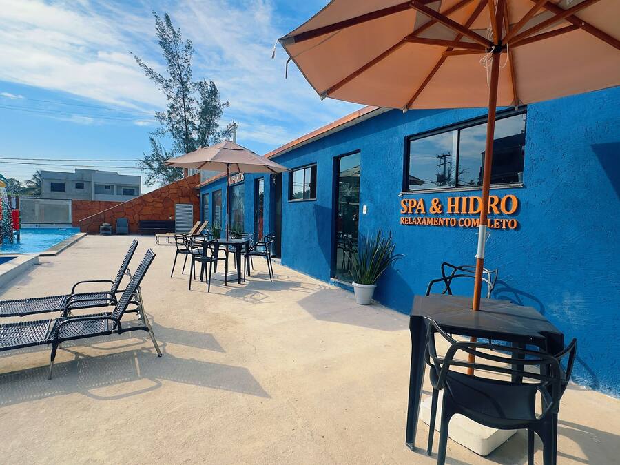 A blue building with a sign for 'SPA & HIDRO' and a pool area with lounge chairs and umbrellas.