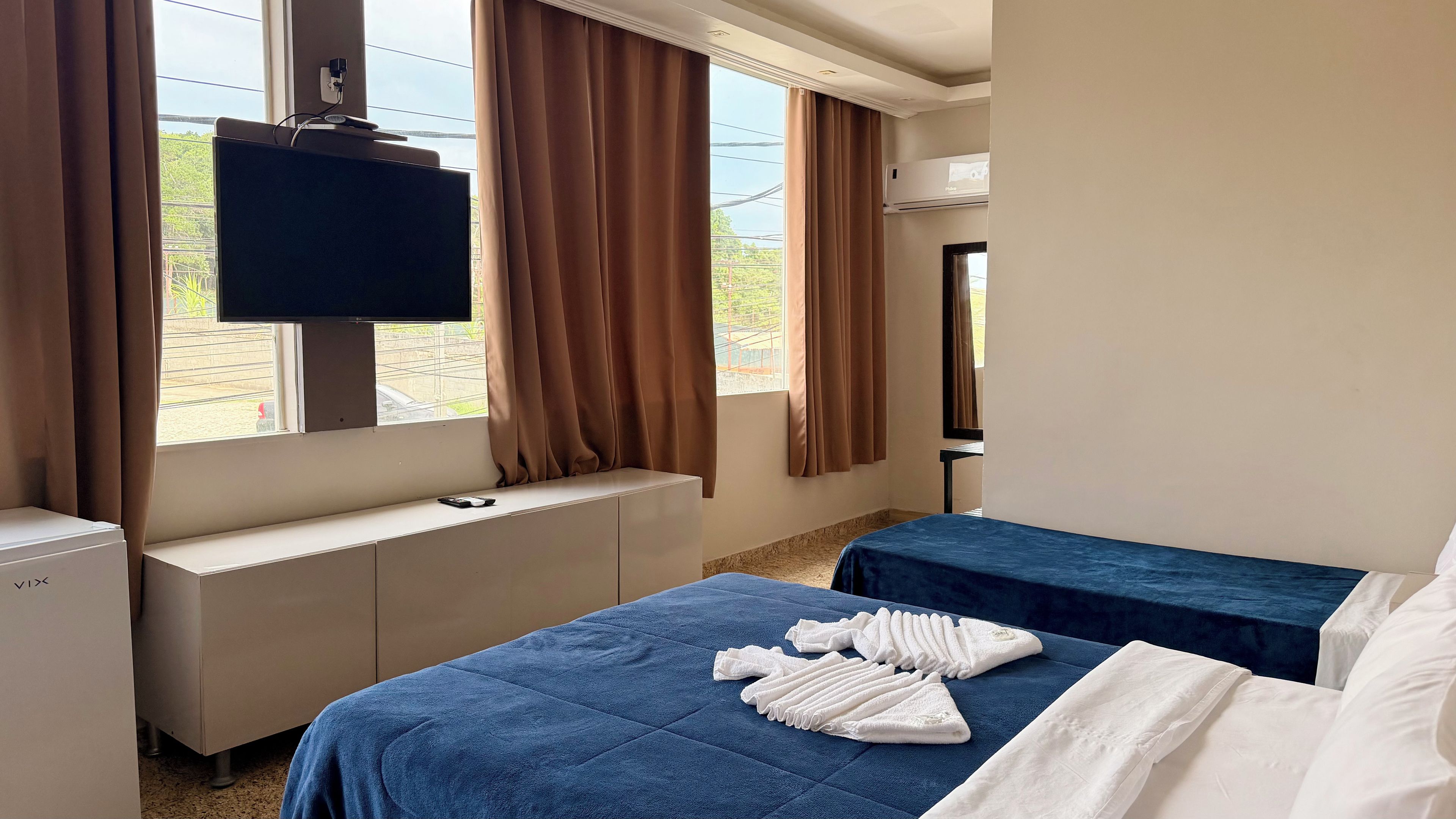 Habitación de hotel con una cama, un televisor montado en la pared, una ventana con cortinas y un radiador.