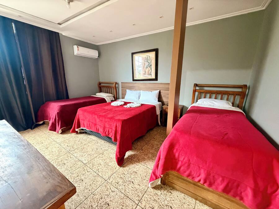 Une chambre d’hôtel avec deux lits simples, une tête de lit en bois, une petite table, une table de chevet et un appareil de climatisation.