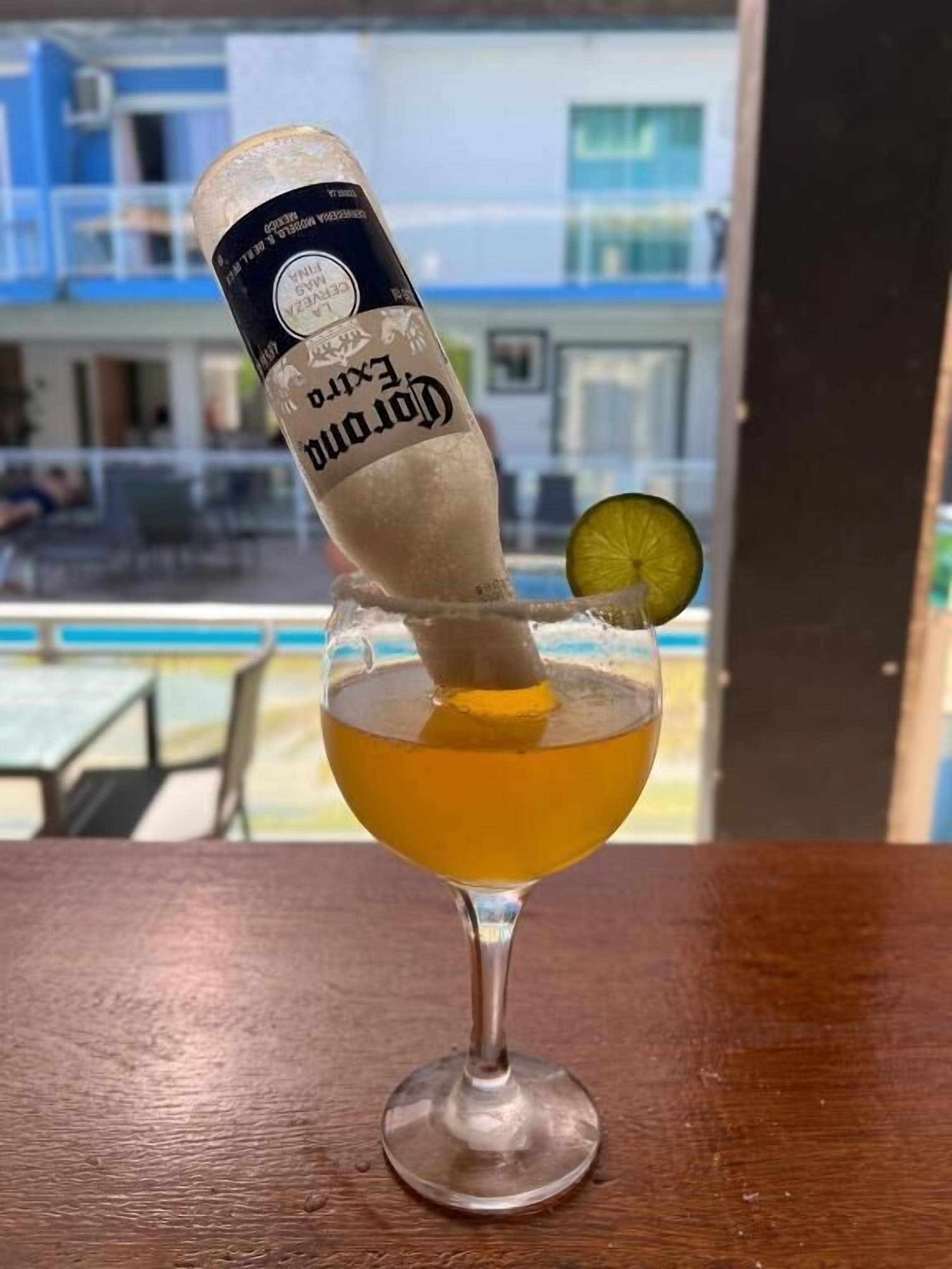 A cocktail with a lime garnish and a bottle labeled "Corona Extra" being poured into it.