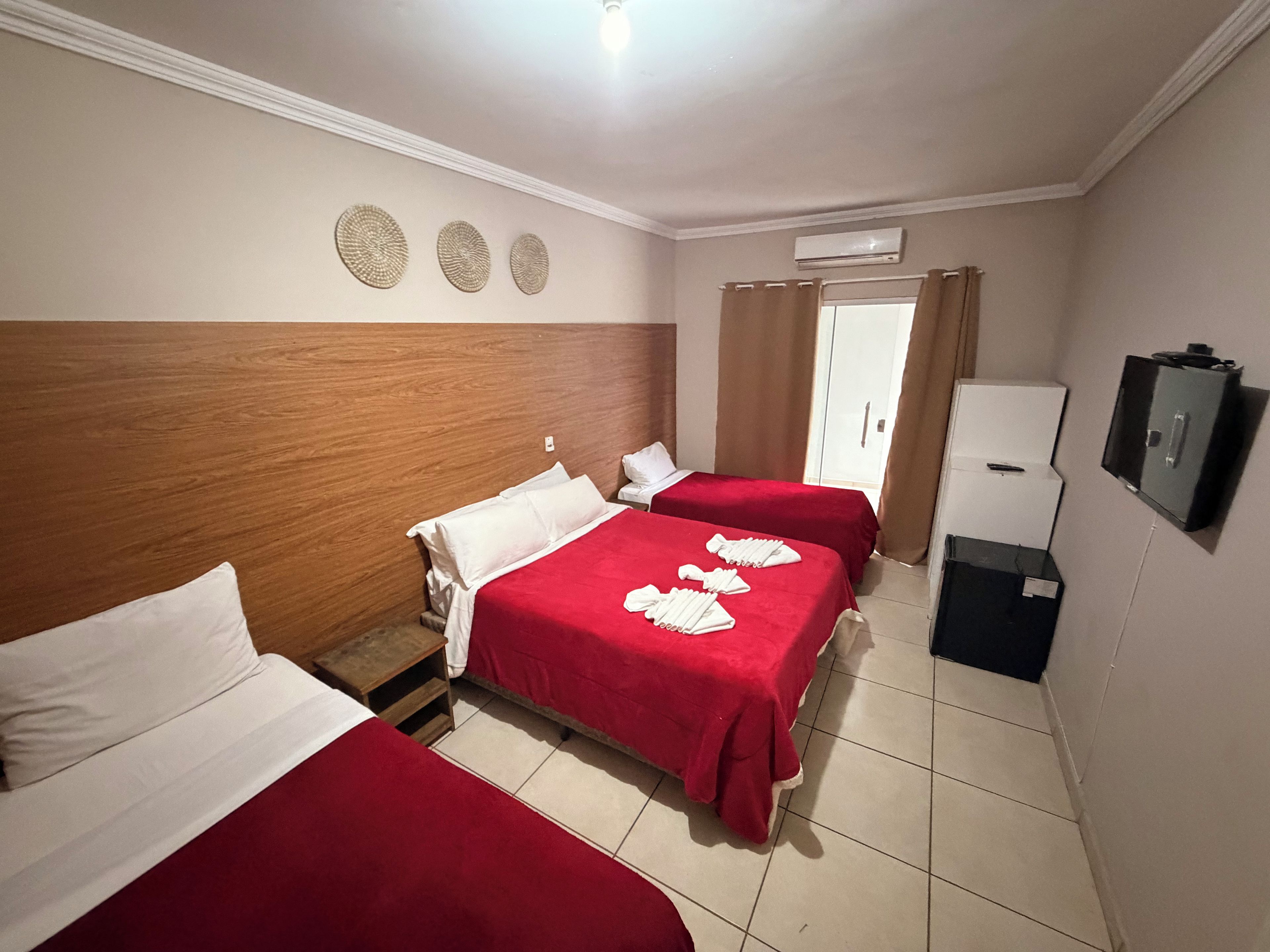 Quarto de hotel com duas camas, um guarda-roupa, uma televisão e ar condicionado.