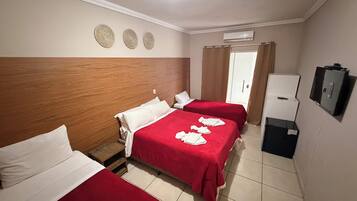 Quarto de hotel com duas camas, um guarda-roupa, uma televisão e ar condicionado.