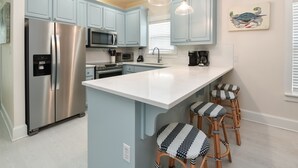 Een moderne keuken met lichtblauwe kastjes, roestvrijstalen apparatuur en een centraal eiland met barkrukken.