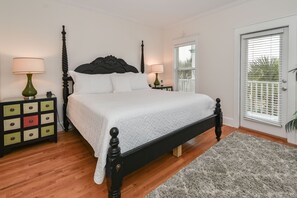Une chambre avec un grand lit, une tête de lit en bois, des tables de chevet avec des lampes, une commode verte et jaune, et un tapis gris.