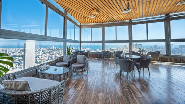 Ein Hochhaus-Interieur mit Holzboden, großen Fenstern mit Blick auf die Stadt, Korbmöbeln und einem polierten Holzboden.