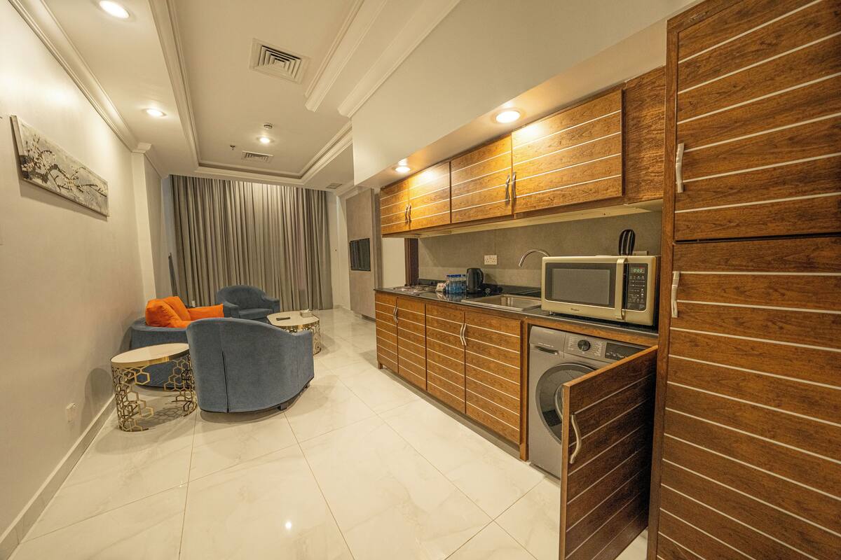Cocina compacta con armarios de madera, microondas y lavadora.