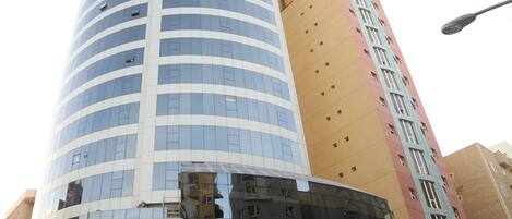 Un hotel moderno con fachada curva, amplias ventanas de vidrio y una entrada destacada con una palmera y zona de estar al aire libre.