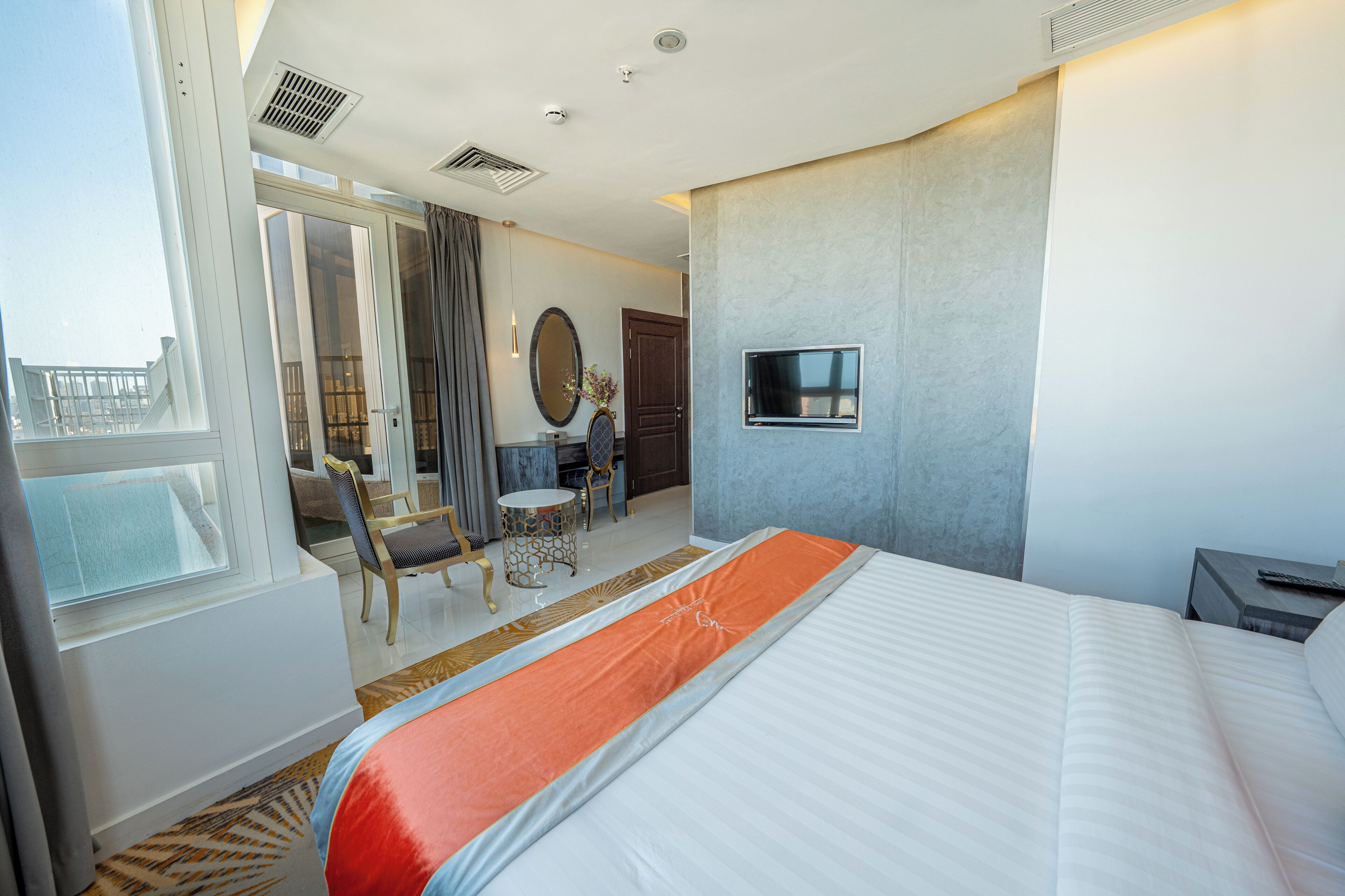 A hotel room with a large bed, a TV mounted on the wall, a balcony with a view, and a seating area with a table and chairs.