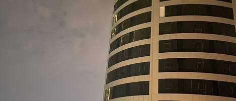 A tall, modern building with a curved facade and a prominent illuminated sign at the top.