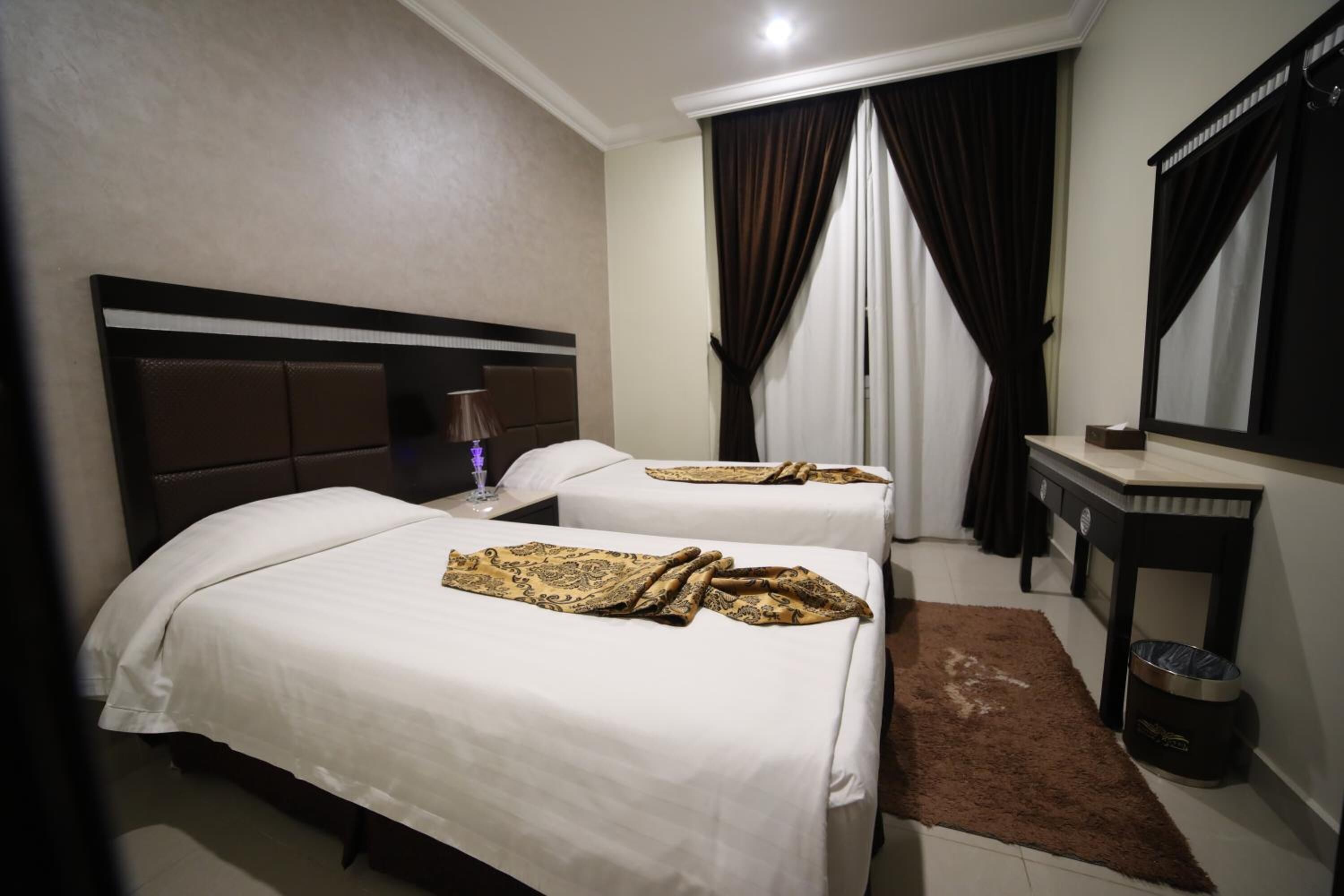 Habitación de hotel con dos camas, una mesita, un espejo y una ventana con cortinas.
