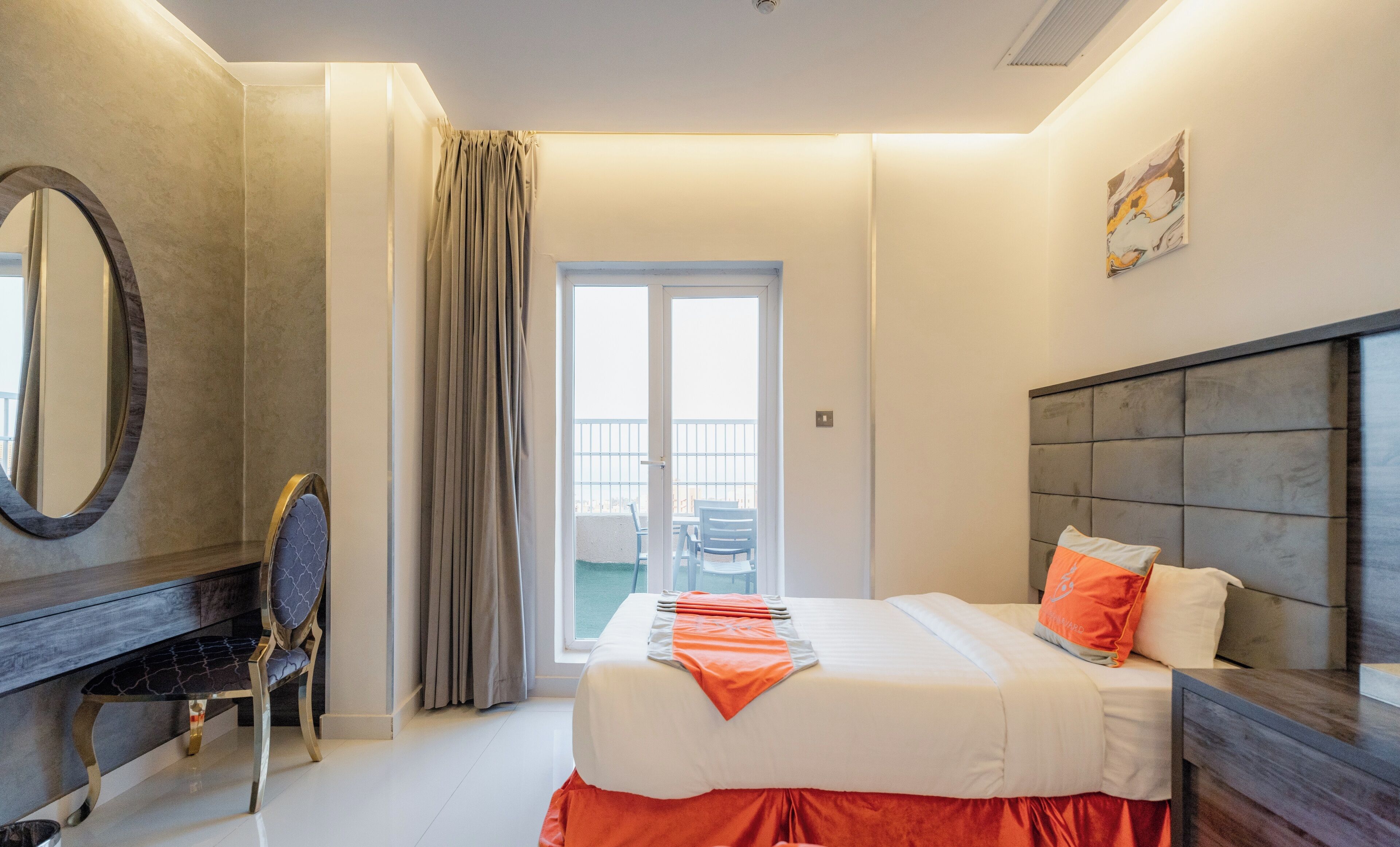A hotel room with a bed, a desk, a chair, a large window with curtains, and a balcony.