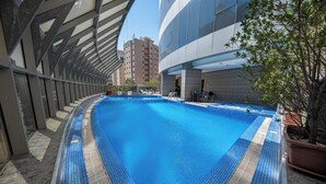 Ein Schwimmbecken mit einer gefliesten Kante, umgeben von einem modernen Gebäude mit großen Fenstern und einem Blumentopf.