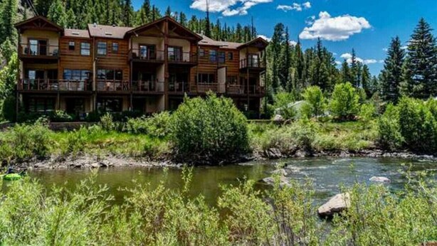 Un'ampia baita di legno con numerosi balconi, situata lungo un fiume con una fitta foresta sullo sfondo.