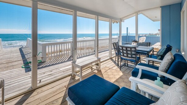 A covered outdoor deck with a view of the ocean, furnished with blue and white chairs and a table. - The Shark and the Seahorse | Ocean Views + Pet-Friendly (Surf City)