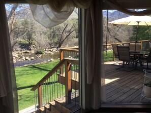 A deck with a table and chairs, overlooking a grassy area and a stream. - "Peaceful Riverfront #1" only 6 miles to park entrance  (Three Rivers)