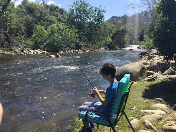 A person sitting on a chair by a river, holding a fishing rod. - "Peaceful Riverfront #1" only 6 miles to park entrance  (Three Rivers)