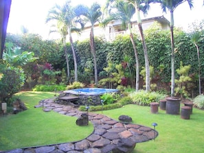 A garden with a swimming pool, stone pathway, and tropical plants.