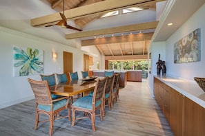 A spacious dining area with a wooden table and wicker chairs, a ceiling fan, and artwork on the walls.