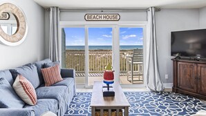 Una sala de estar con un sofá azul, una mesa de centro con un adorno, un televisor y un balcón con vista a la playa.