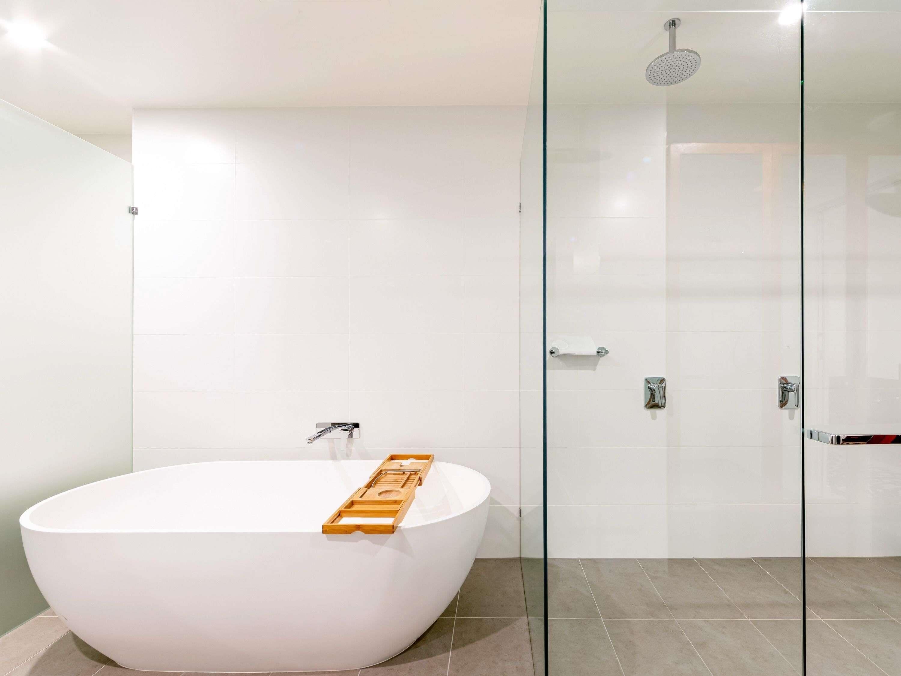 Ein modernes Badezimmer mit einer freistehenden Badewanne, einer Duschkabine aus Glas und einer Holzauflage in der Wanne.