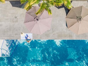 A swimming pool with two umbrellas, a tiled deck, and a person relaxing on a striped towel. - Novotel Brisbane South Bank Hotel (South Brisbane)