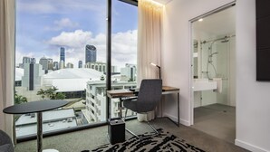 A modern hotel room with a city view, a desk, a chair, a glass shower, and a large window. - Novotel Brisbane South Bank Hotel (South Brisbane)