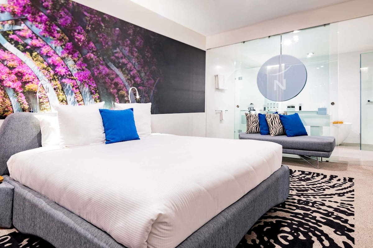 Un dormitorio moderno con una cama grande, un sofá, un separador de vidrio y una pared con un mural floral.