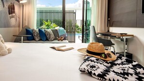 A modern hotel room with a large bed, a desk, a chair, a sofa with patterned cushions, a straw hat, and a book. - Novotel Brisbane South Bank Hotel (South Brisbane)
