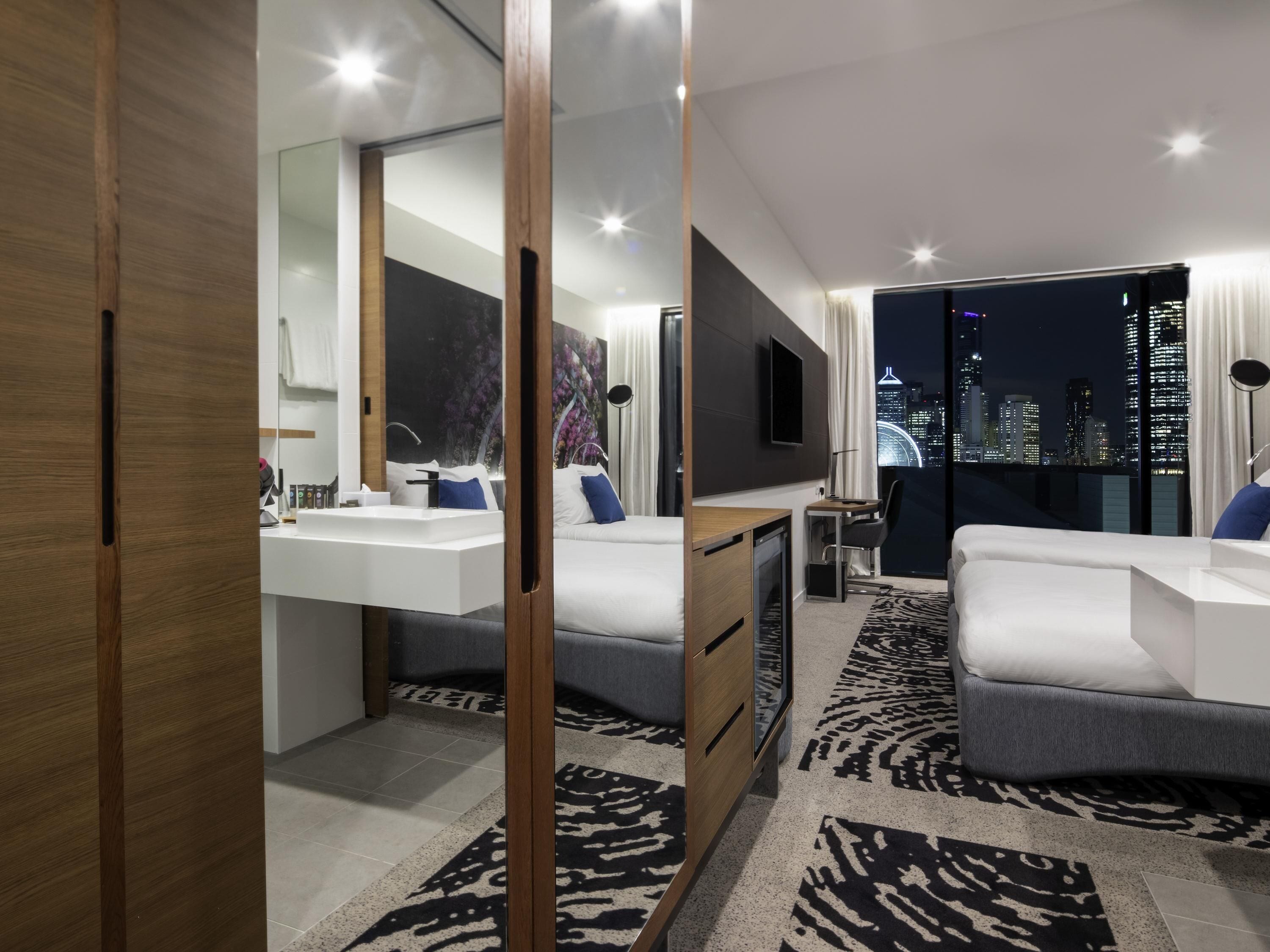 Une chambre d’hôtel moderne avec vue sur la ville, un grand miroir, un téléviseur à écran plat, un bureau et un canapé.