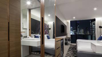 Une chambre d’hôtel moderne avec vue sur la ville, un grand miroir, un téléviseur à écran plat, un bureau et un canapé.