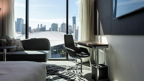 A modern hotel room with a large window offering a city view, a bed, a sofa, a desk, and a chair. - Novotel Brisbane South Bank Hotel (South Brisbane)