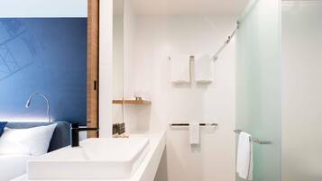A modern bathroom with a large white sink, a shower, and a glass shower door.