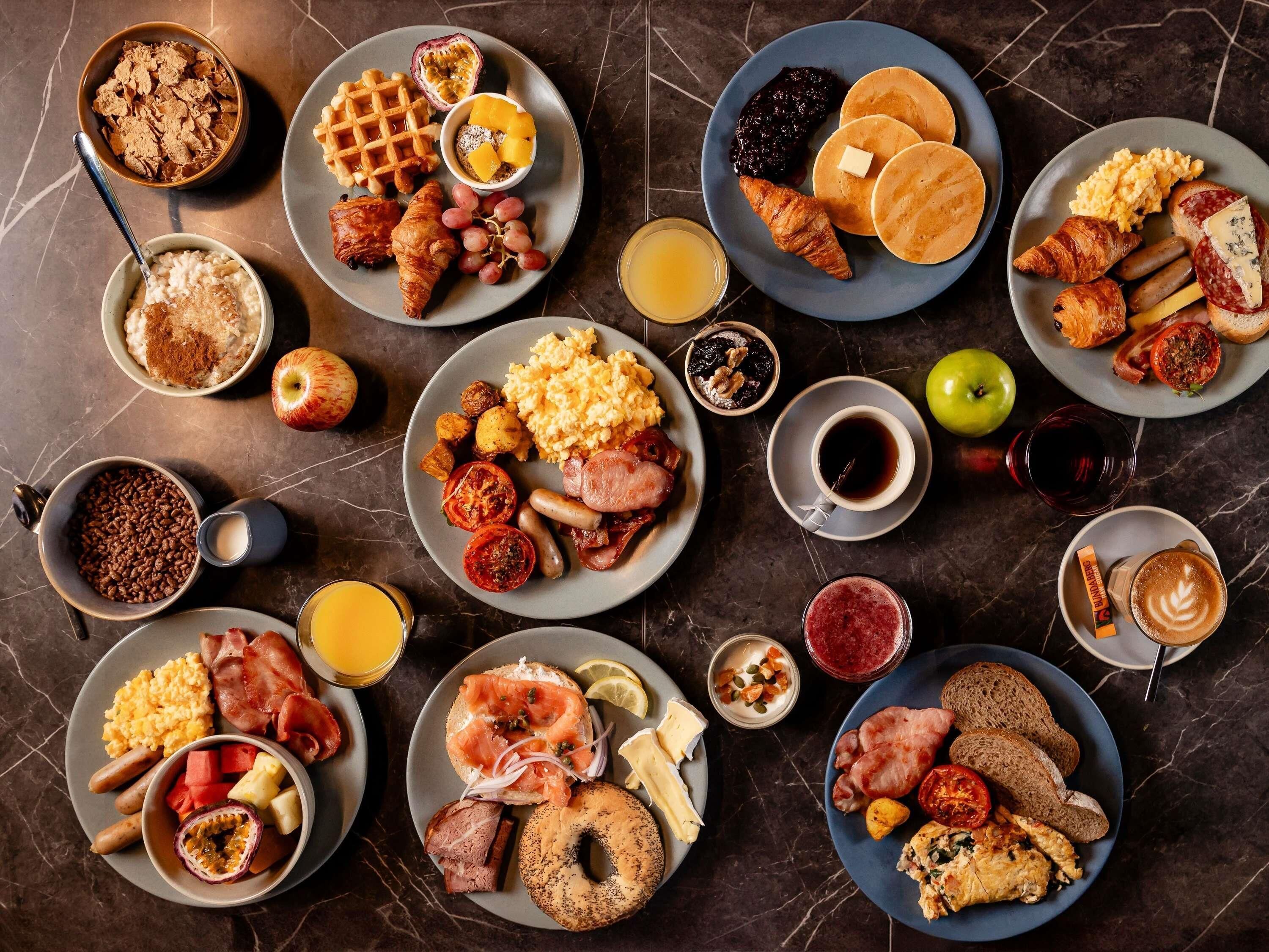 A variety of breakfast dishes arranged on plates, including waffles, pancakes, eggs, and pastries.