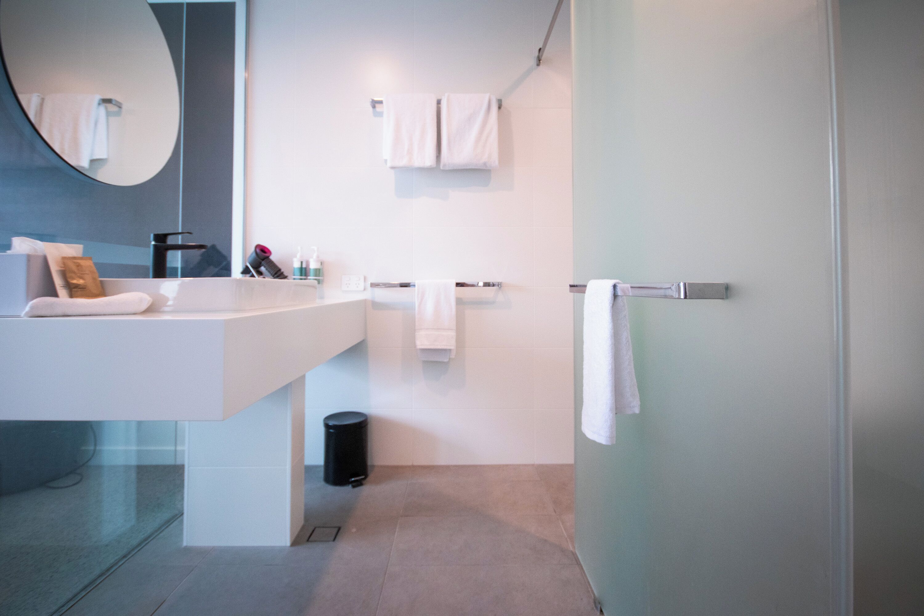 Une salle de bain moderne avec un grand miroir, un lavabo blanc et deux porte-serviettes.