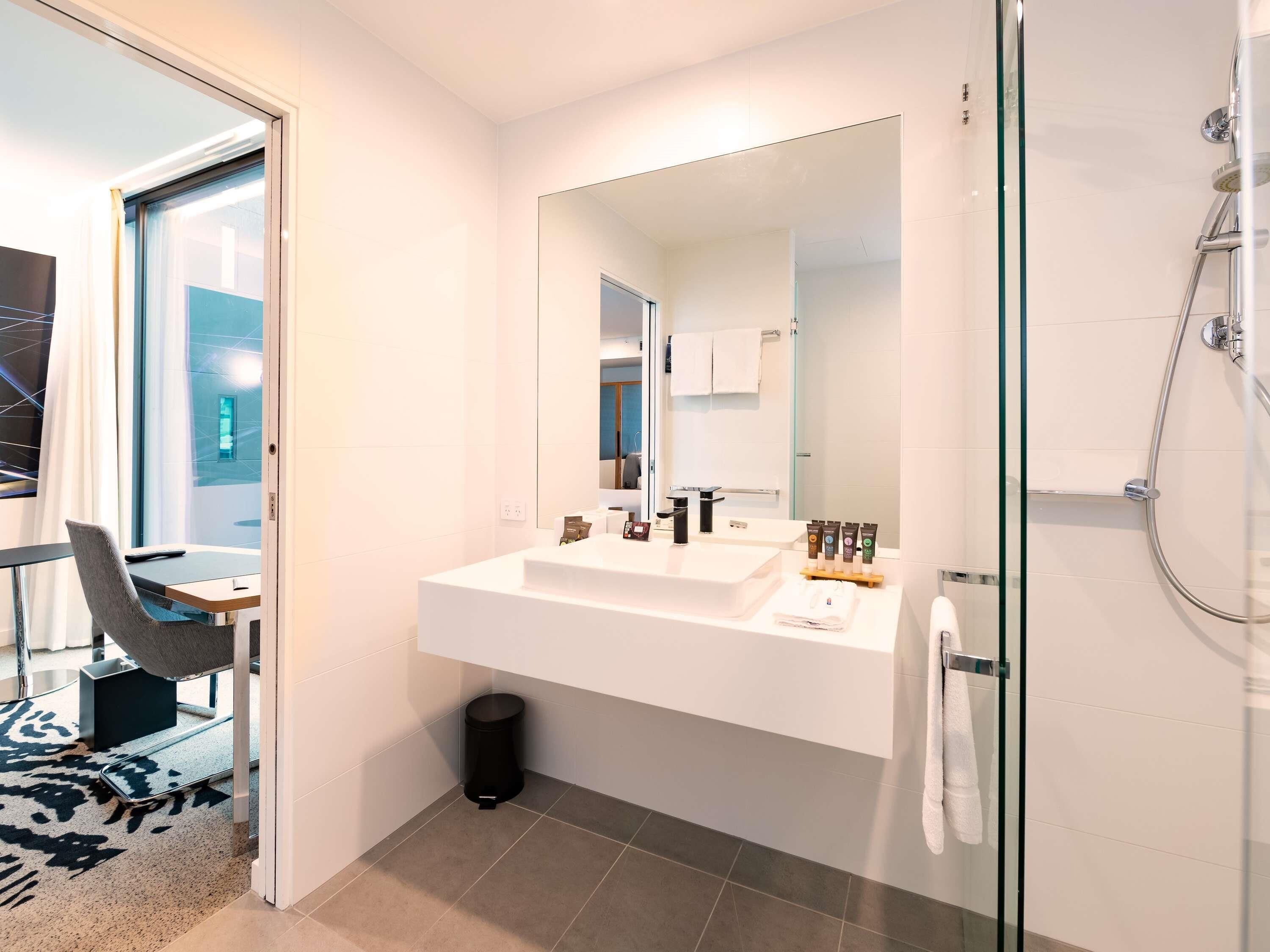 Un baño moderno con un espejo grande, dos lavamanos, una ducha y un ventanal de vidrio que da a un balcón.