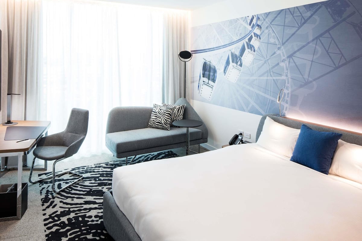 Habitación de hotel con cama, escritorio, silla, sofá y pared con diseño geométrico.